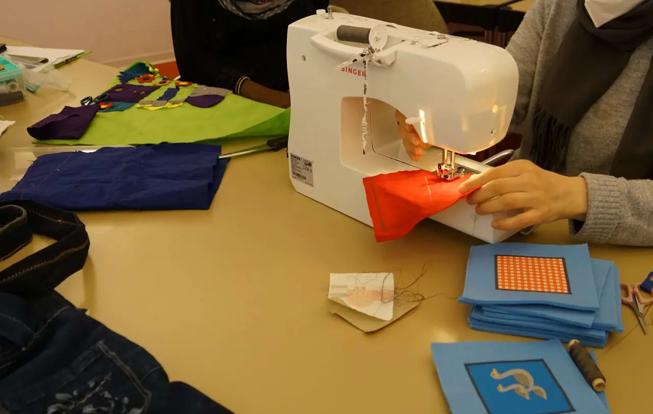 Suzan näht Bilder auf viereckige Stoffstücke.