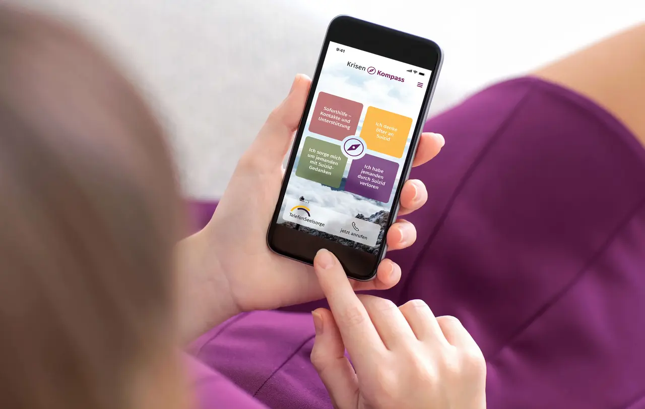 woman purple dress holding phone with home screen icons apps Die KrisenKompass App ist jederzeit und in Griffweite dabei, wenn mentale Hilfe nötig ist.