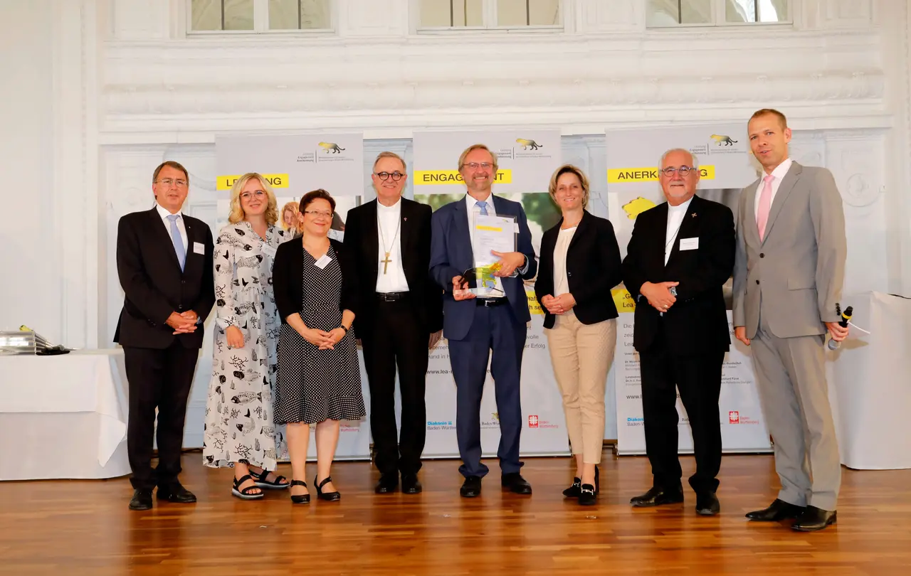 Für die Bäckerhaus Veit GmbH aus Bempflingen nahm Johannes Klümpers die Auszeichnung entgegen. Links neben ihm (v.l.n.r.) Oberkirchenrat Dieter Kaufmann (Vorstandsvorsitzender des Diakonischen Werks Württemberg, Bettina Schmauder (Bund der Selbstständigen Baden-Württemberg e. V.), Dr. Anette Holuscha-Uhlenbrock (Vorstand des Caritasverbandes der Diözese Rottenburg-Stuttgart) und Landesbischof Dr. h. c. Frank Otfried July. Rechts neben ihm Wirtschaftsministerin Dr. Nicole Hoffmeister-Kraut, Bischof Dr. Gebhard Fürst und Moderator Helge Thun.