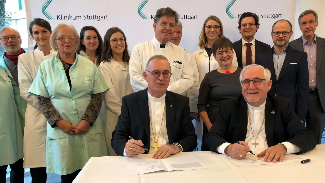 Januar 2020, die Corona-Krise war noch weit: Landesbischof Dr. h. c. Frank Otfried July (sitzend, links) hat mit Bischof Dr. Gebhard Fürst im Klinikum Stuttgart die Rahmenvereinbarung zur ökumenischen Klinik-Seelsorge unterzeichnet. Direkt hinter July beobachten der Ärztliche Direktor der Klinik für Allgemeine Innere Medizin, Professor Dr. Wolfram G. Zoller, und sein Team die Szene. Zu den Beobachtern der Unterzeichnung gehörten auch der Medizinische Vorstand am Klinikum, Professor Dr. Jan Steffen Jürgensen (hintere Reihe, 3. v. r.) und Pfarrer Thomas Dreher, Vorsitzender des Konvents der Evangelischen Krankenhaus- und Kurseelsorge Württemberg (r.)