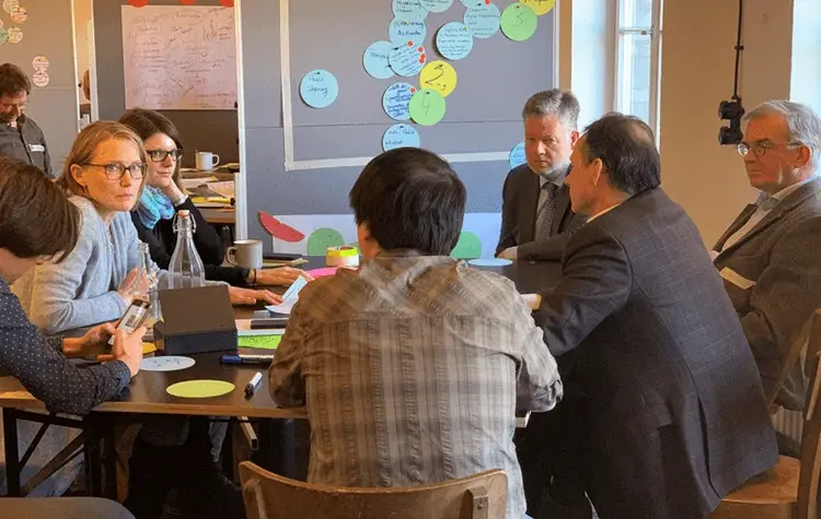 EthicalDesignSprint_Personengruppe_Workshop_032020_ELKW Personengruppe sitzt an Tisch, im Hintergrund Pinnwand mit Klebezetteln